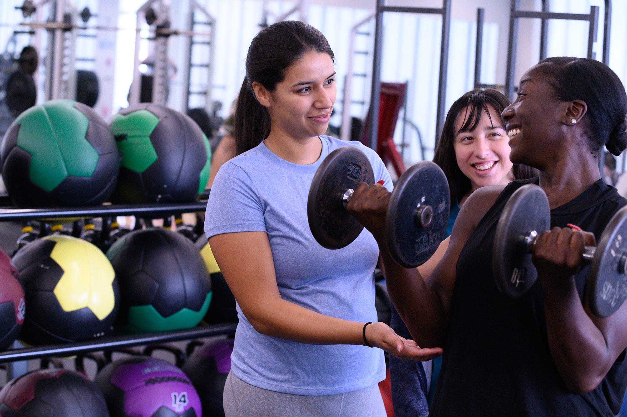 A fitness instructor works with at student who is curling a dumbbell