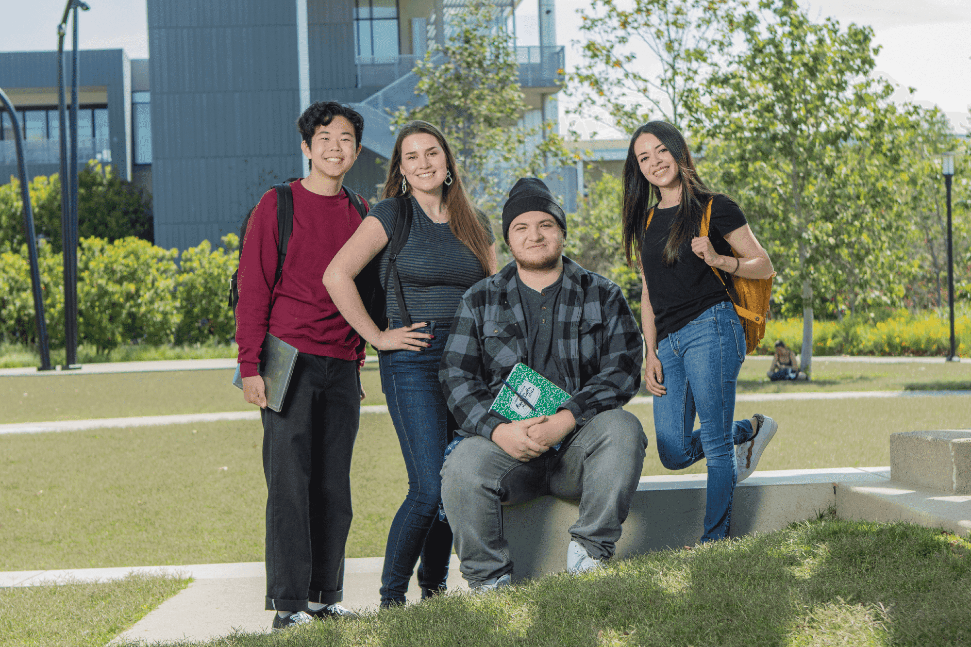 Four Promise students with books and backpacks outside on a bench with grass and trees in the background.