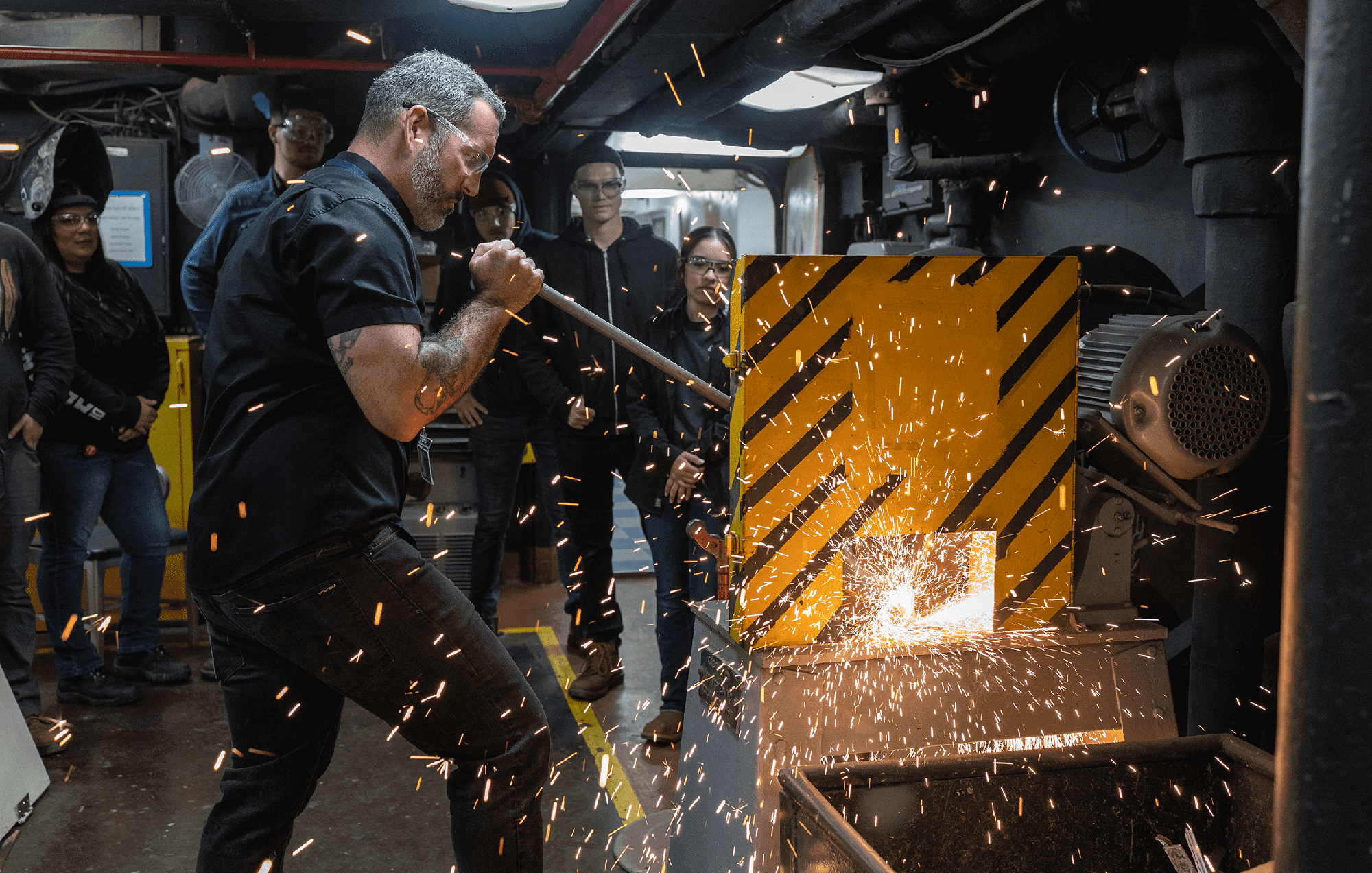 Sparks fly as students watch in instructor work on welding equipment