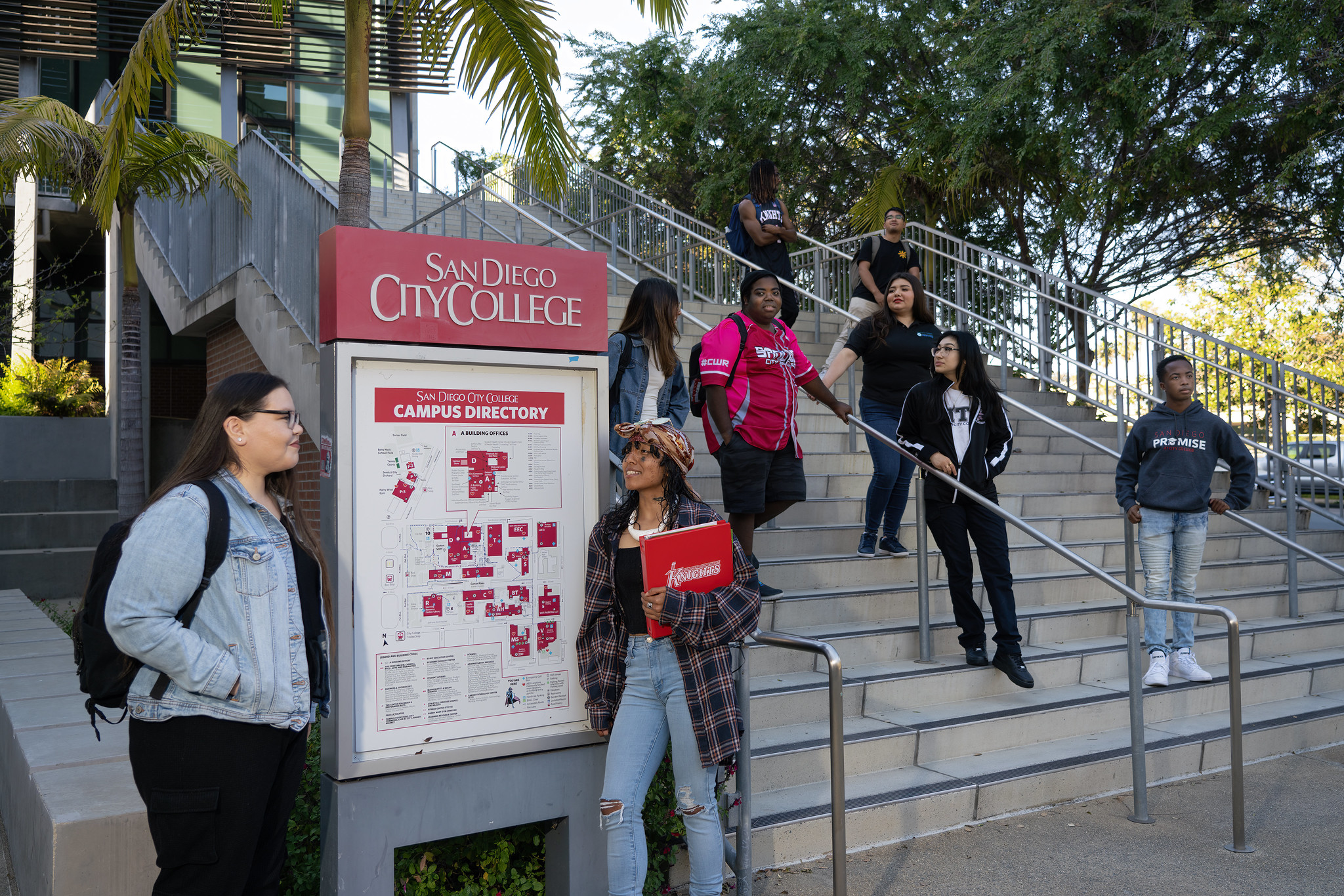 A group of students on stairs and near a campus directory sign outside at the City College campus