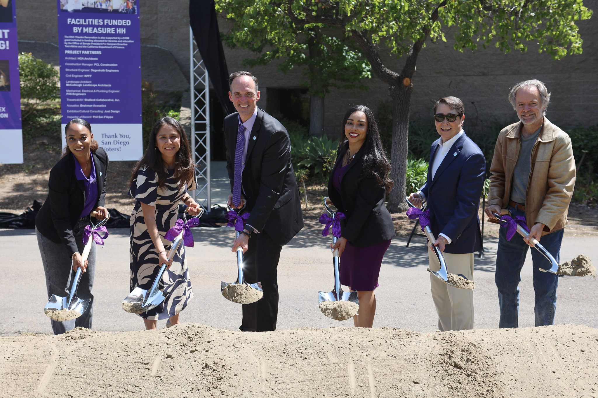 Six district officials hold shovels and dig into a pile of dirt at a groundbreaking ceremony