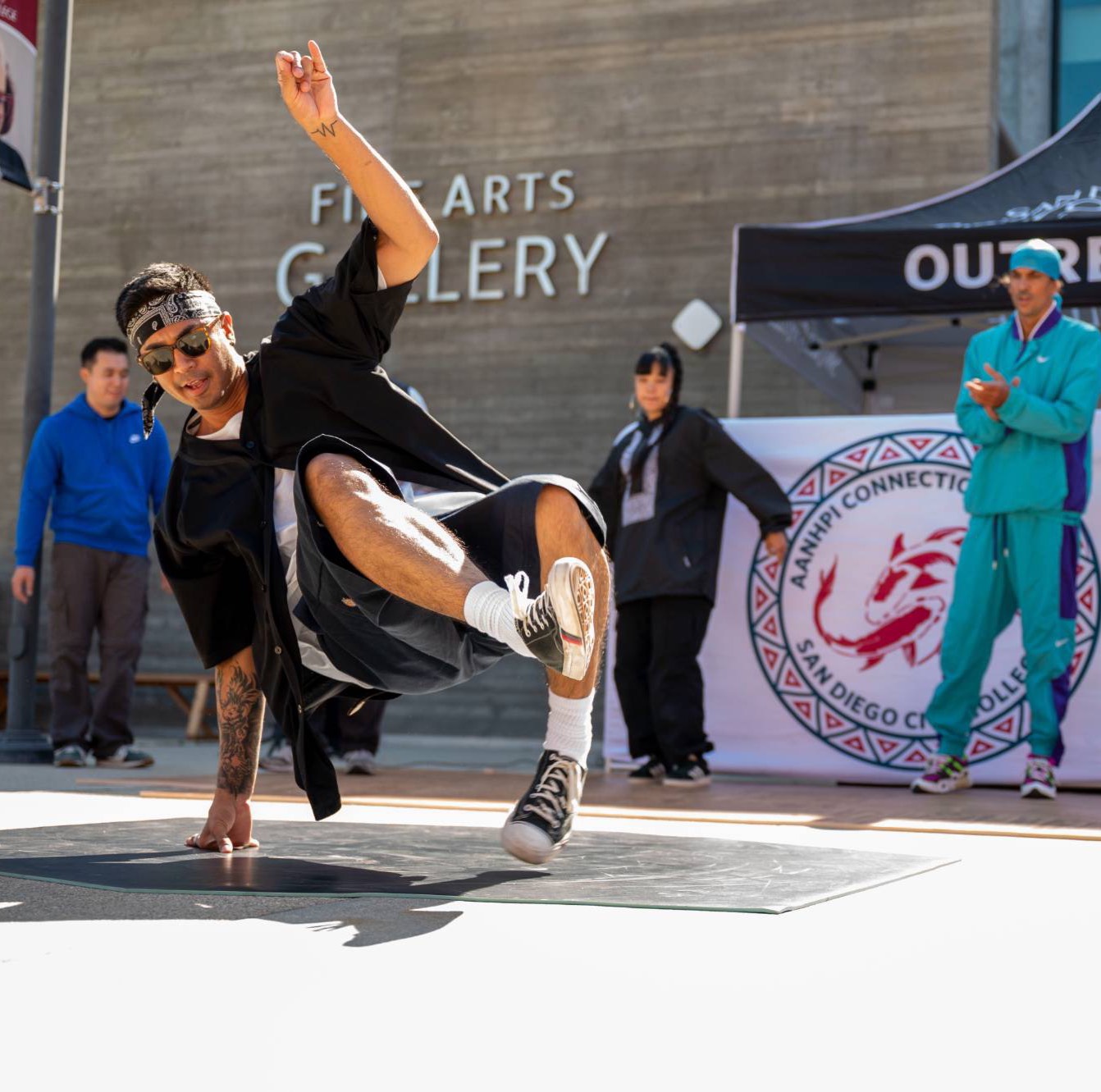 Three people watch a man breakdancing on campus