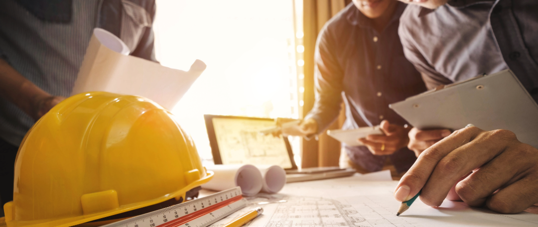 Three people look over blueprints spread out on a table.