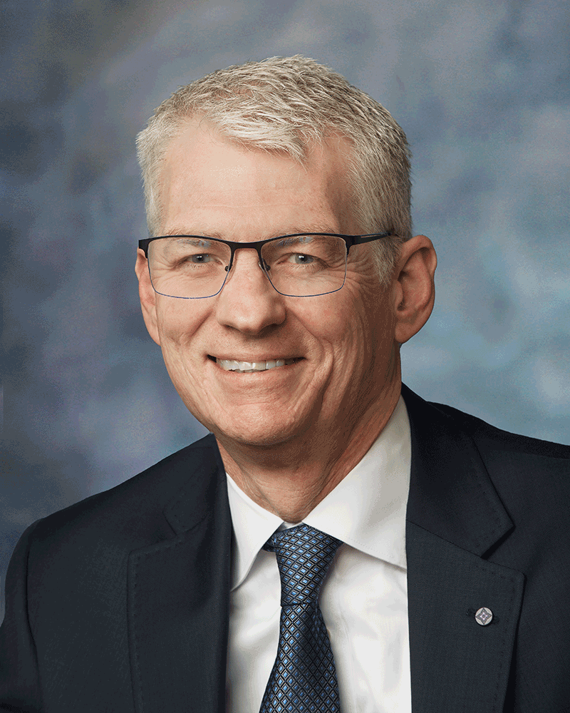 Daniel Troy is wearing a black suit and a blue tie in a portrait photo
