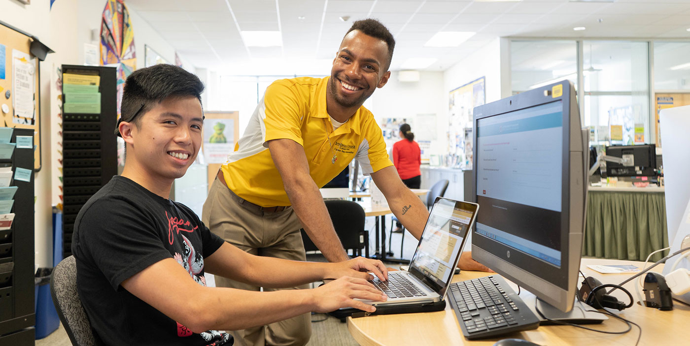 A student sits at a desk in the career center. An employee at the center is helping him.