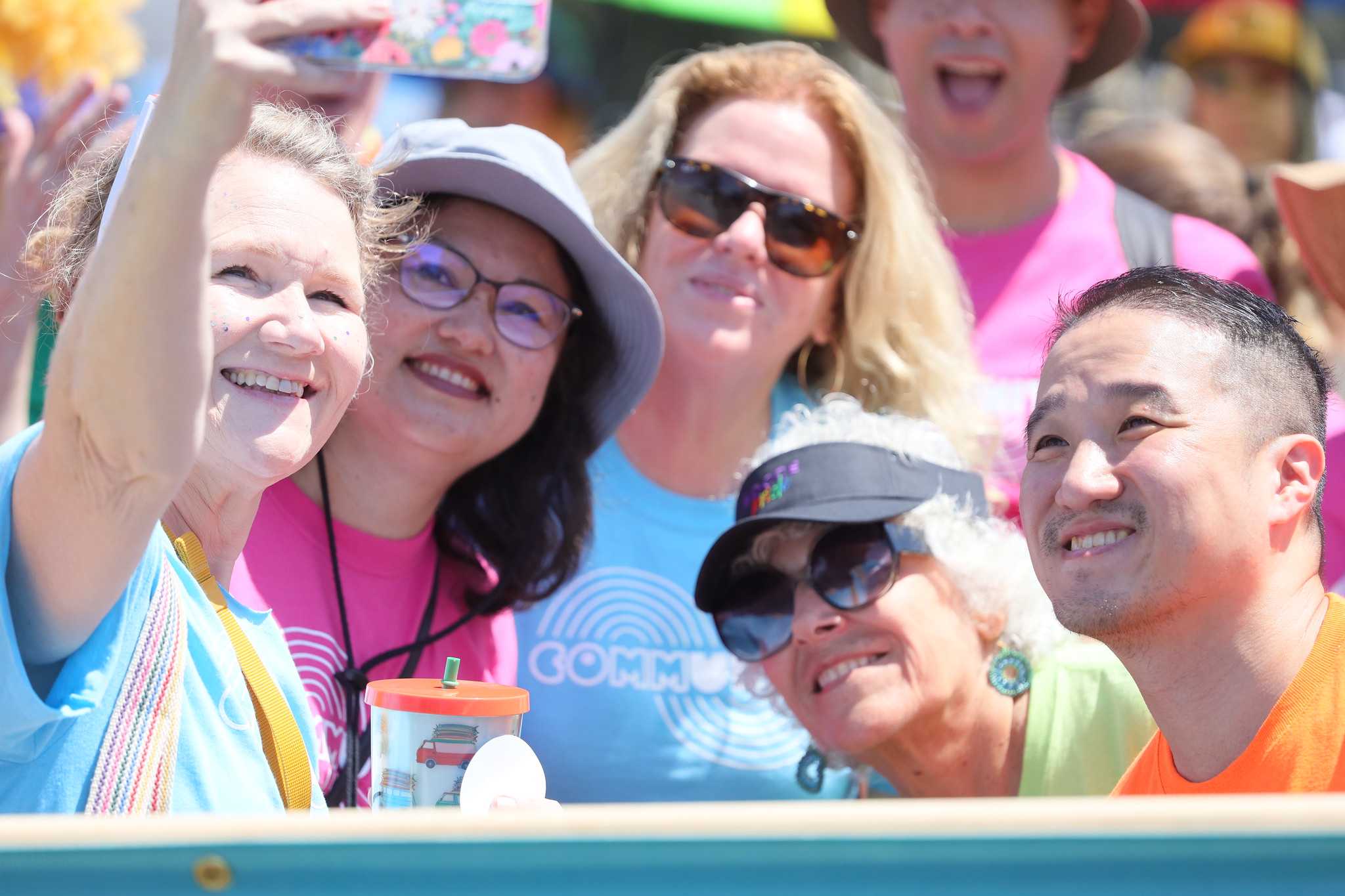 Five employees in pink blue and green tee shirts take a selfie at the pride parade