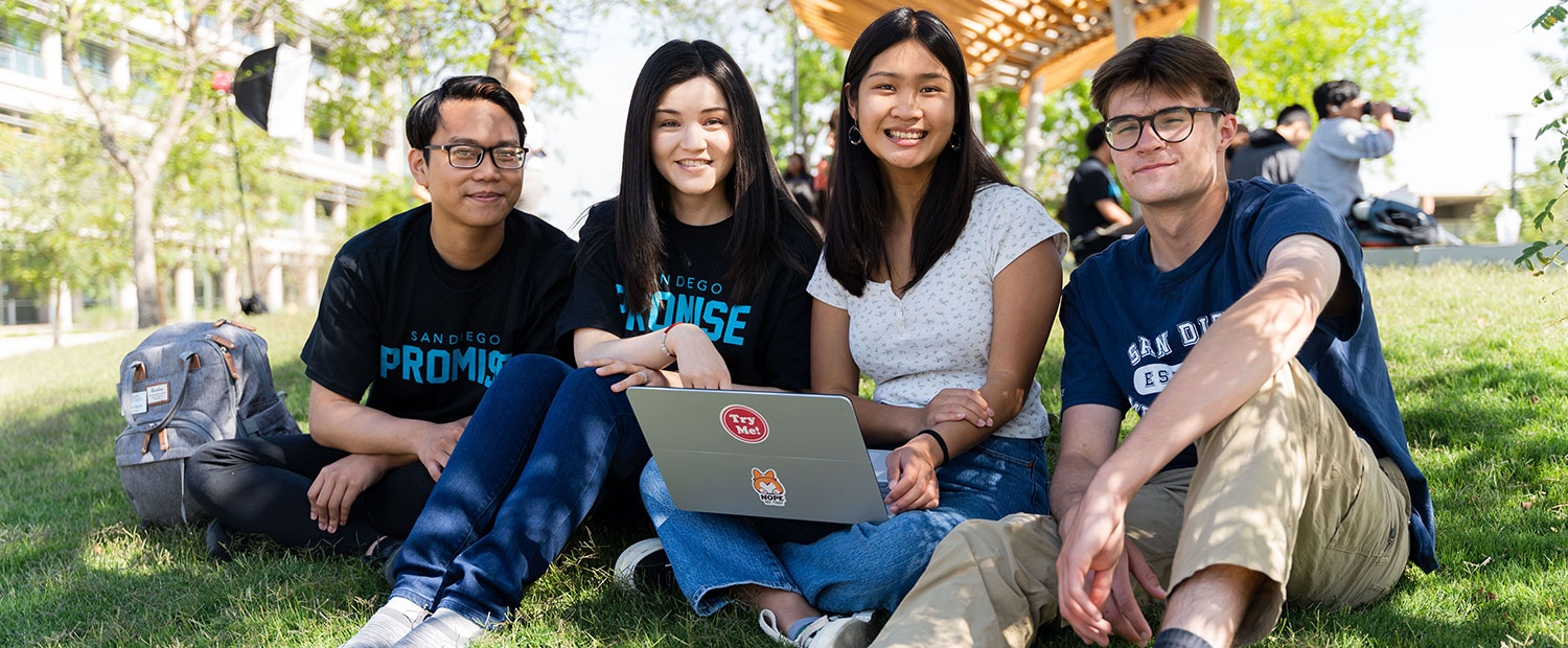 Four students on the grass looking at a laptop