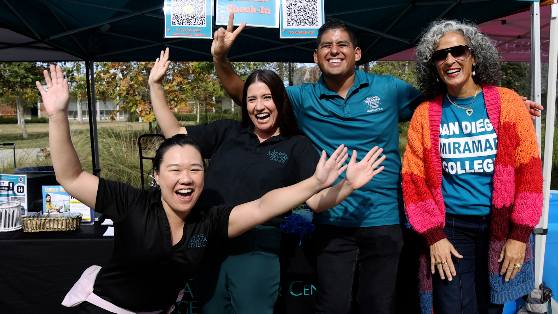 Four people wearing Miramar tee shirts in front of a welcome booth