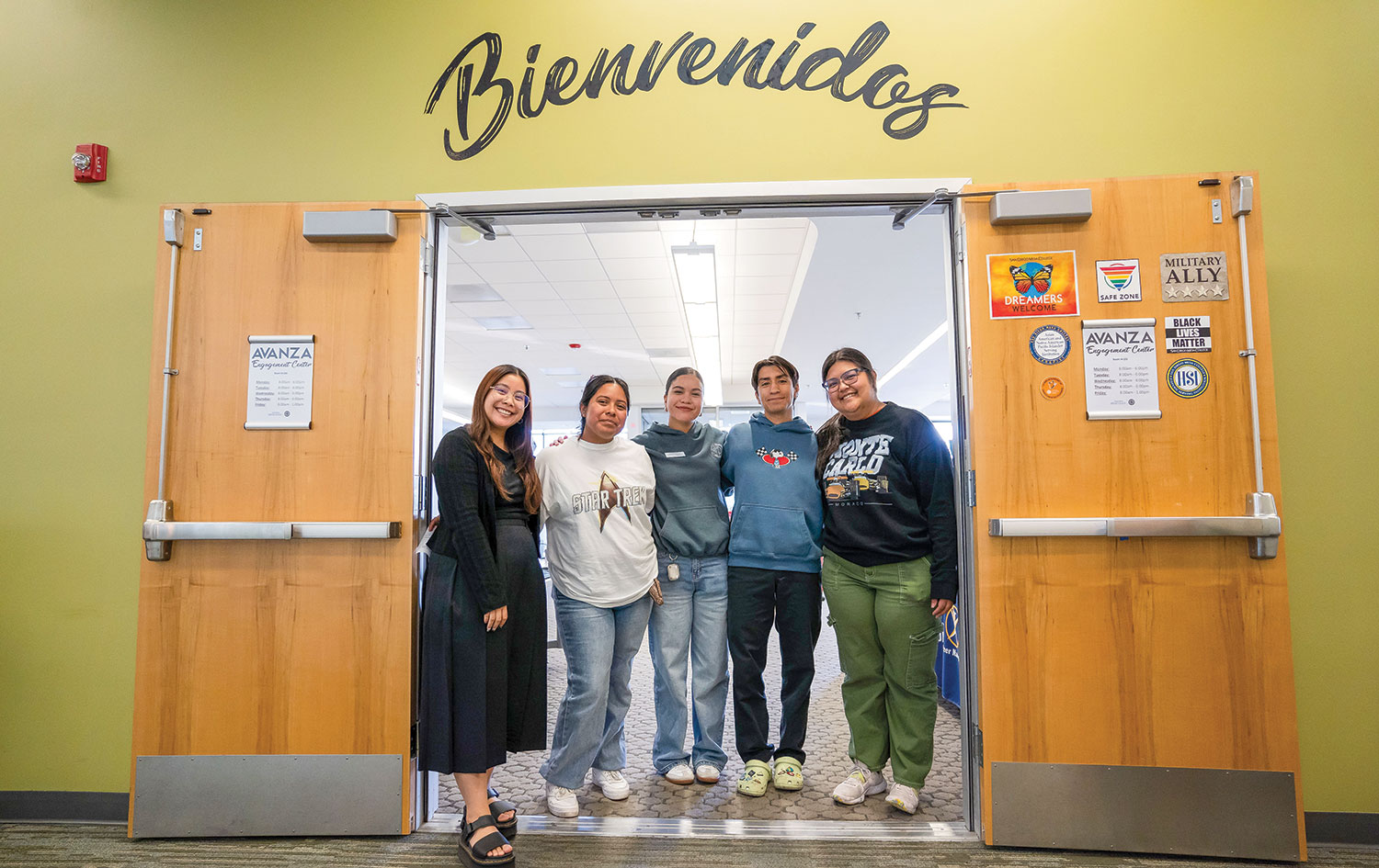 Five people stand in a doorway the word bienvenidos above the doors