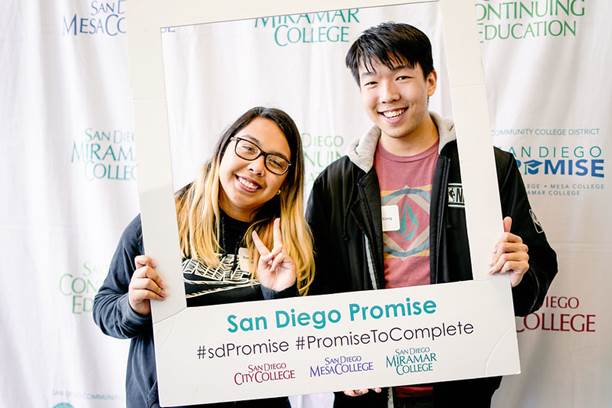 Two students hold up a white frame that says San Diego Promise