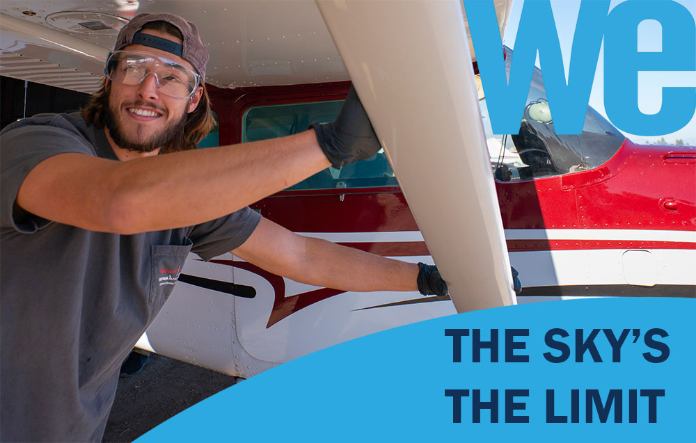 Cover of WE magazine shows a student wearing gloves and protective goggles pushing a white and red plane on a runway