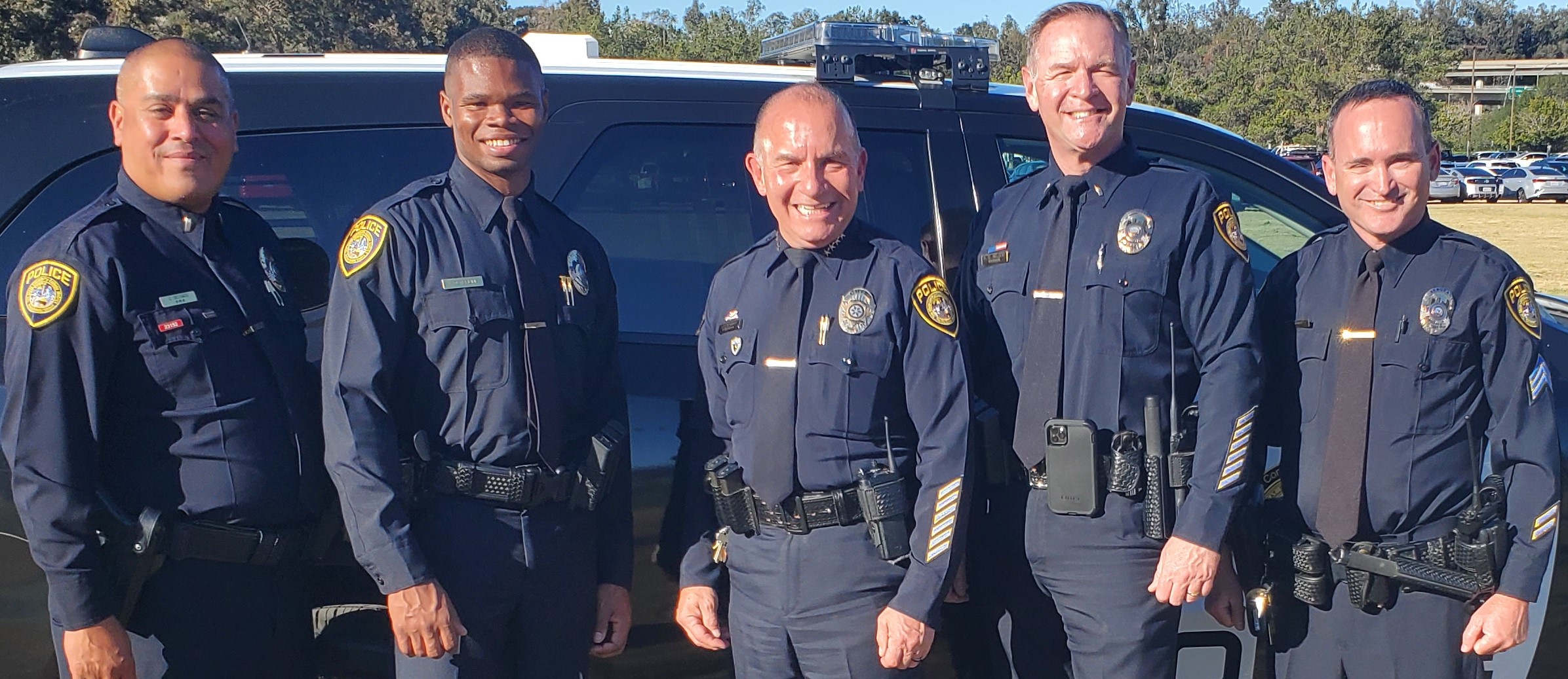 Four officers and the chief all in uniform standing next to a police SUV