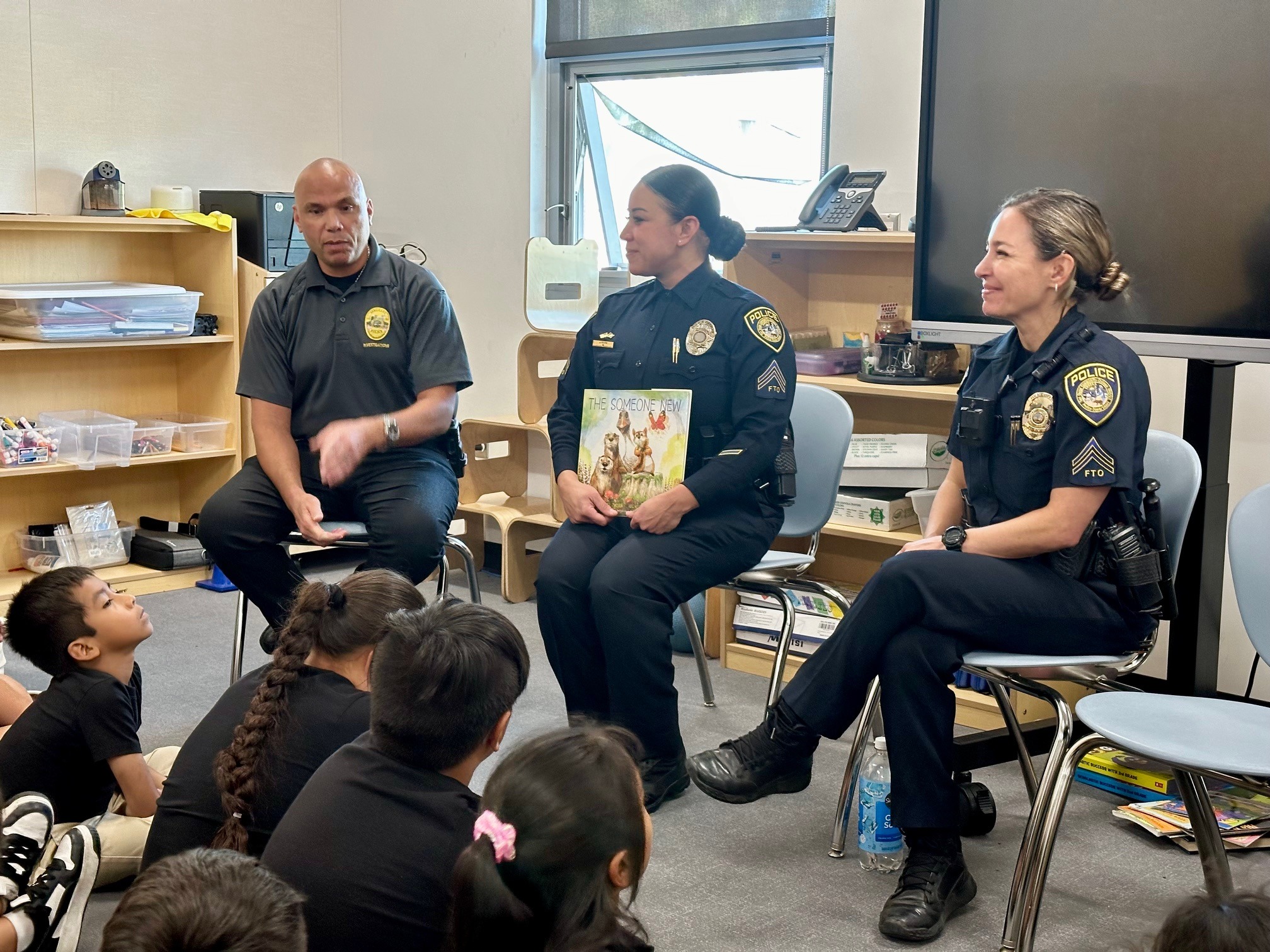 Three college police officers read a book to a classroom of children