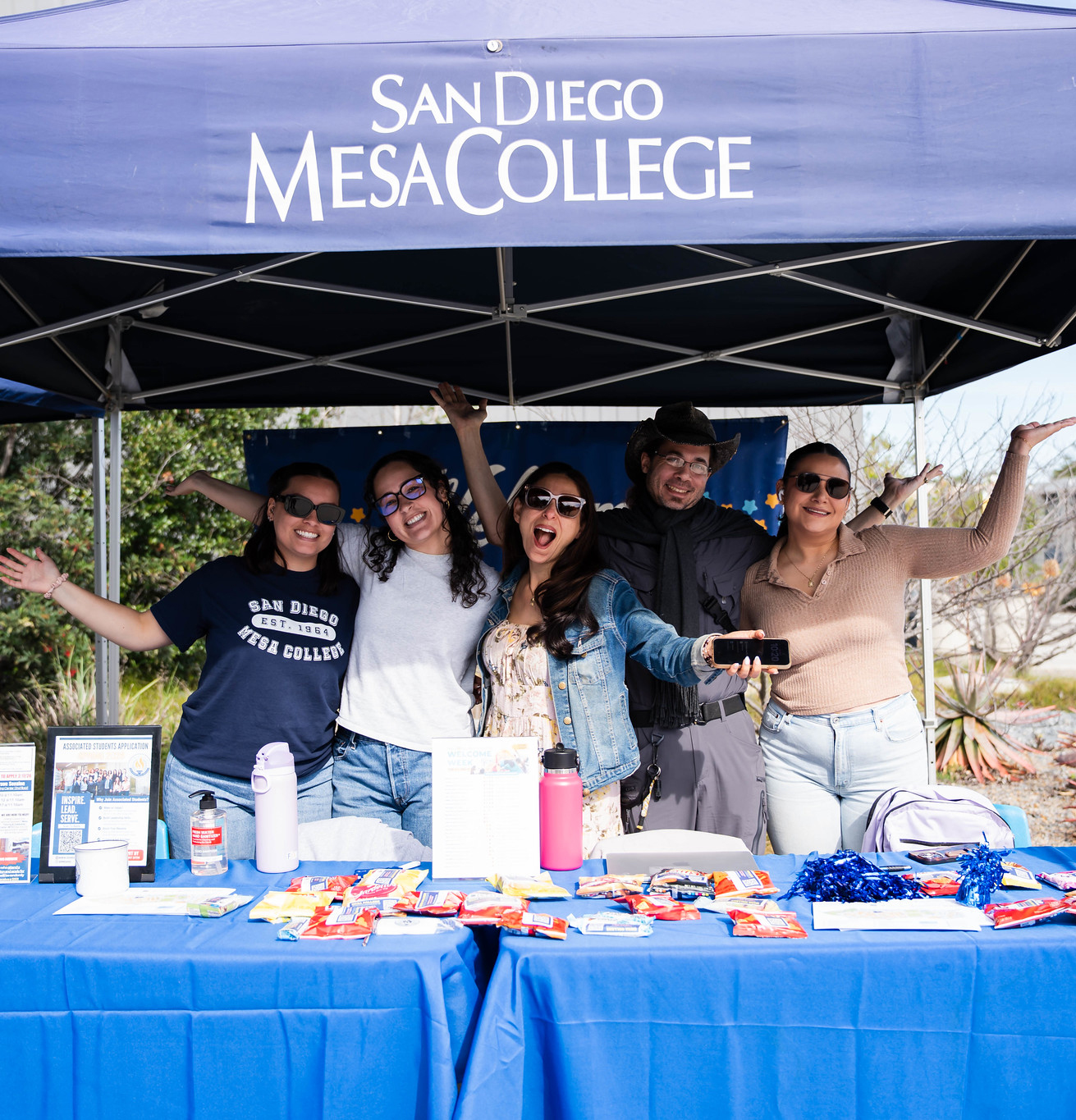 
Five people pose with their hands in the air for a group photo.
